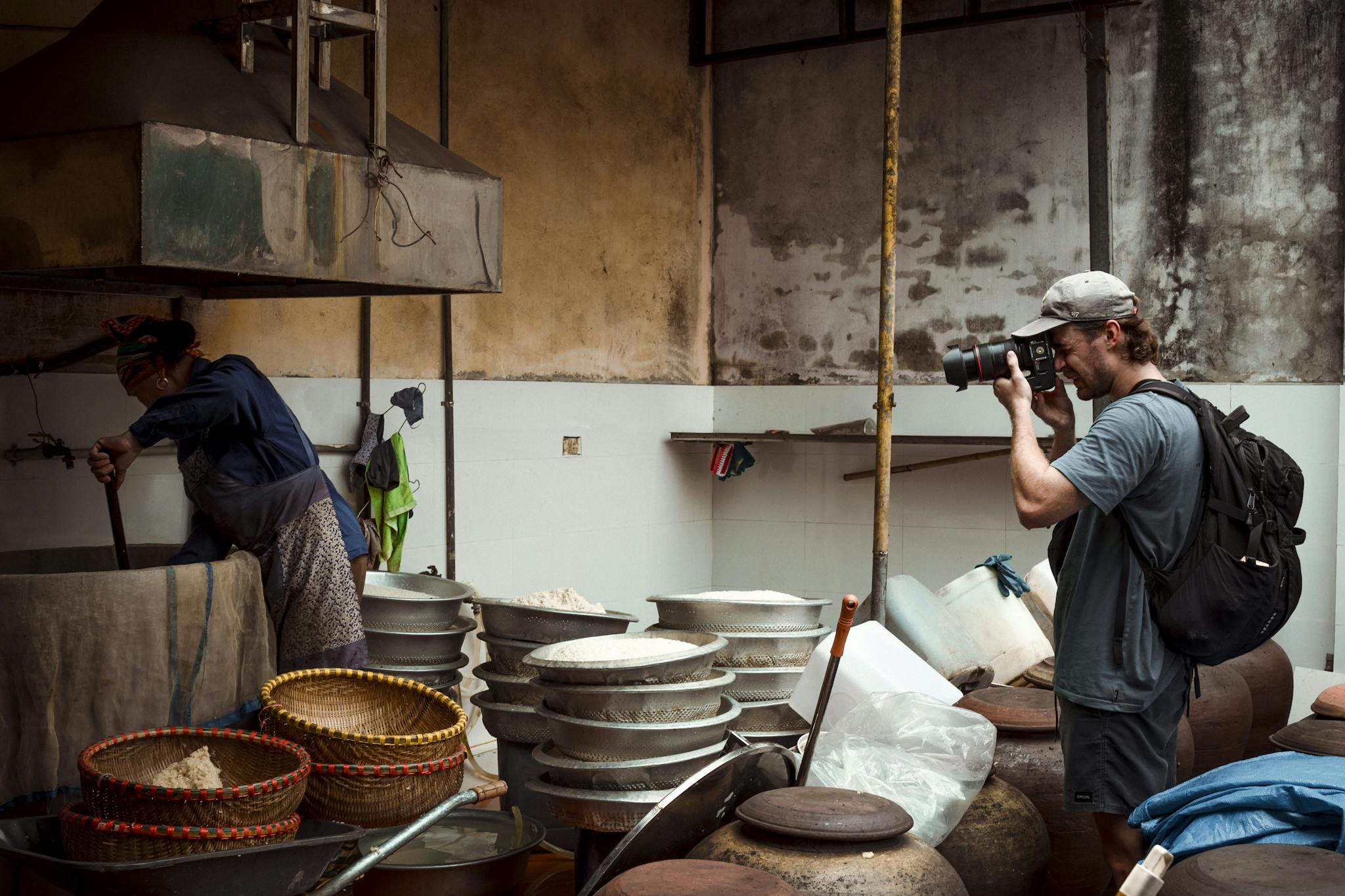 A photographer documents a traditional artisan cooking in a rustic kitchen environment.