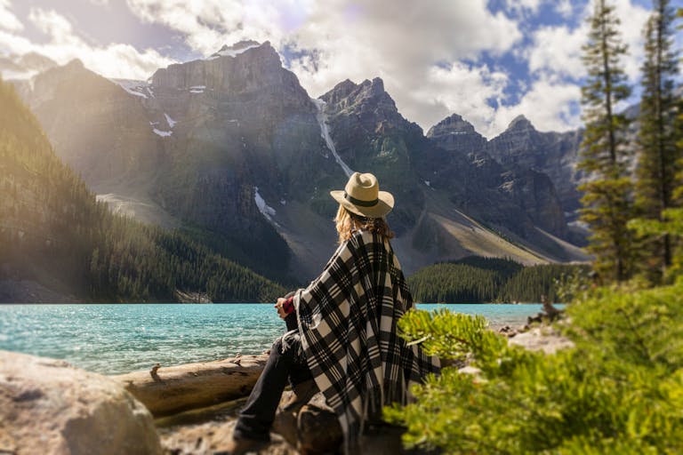 Woman in a poncho gazing at Moraine Lake surrounded by mountains, Alberta, Canada.